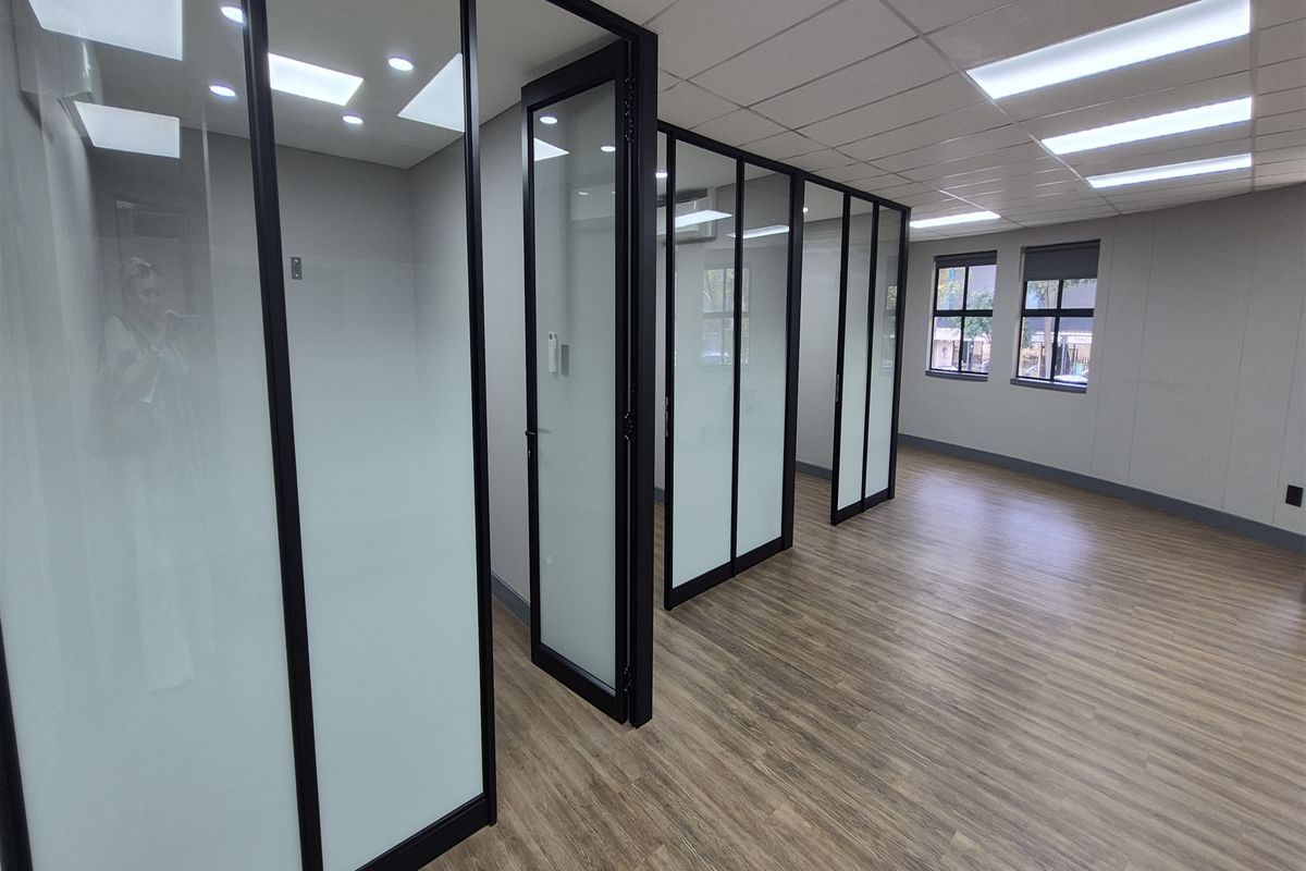 Modern office space featuring glass partition walls, suspended ceilings with recessed lighting, and durable laminate flooring in a clean, professional environment.