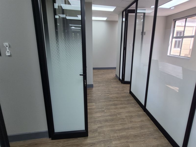 Modern office space featuring glass partition walls with black aluminum frames, frosted privacy film, and durable wood-look flooring.
