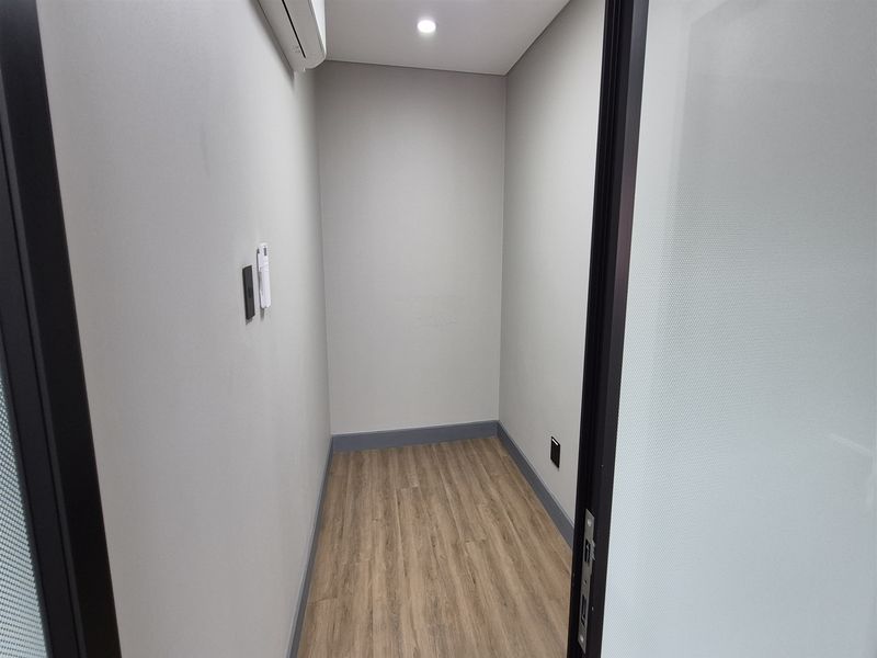 A clean, empty office space featuring modern laminate wood flooring, recessed lighting, and a split-system air conditioning unit.
