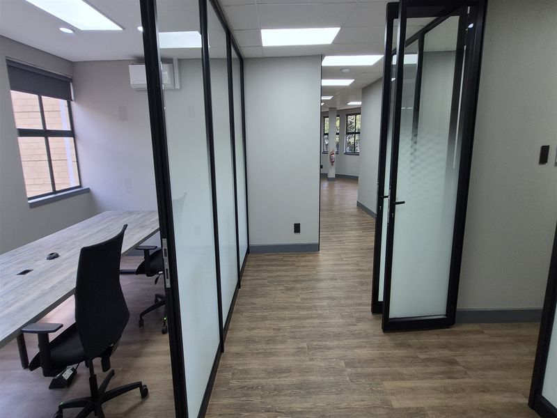 Modern office space featuring glass partition walls, black metal framing, recessed lighting, and durable wood-look flooring in a professional, well-maintained environment.