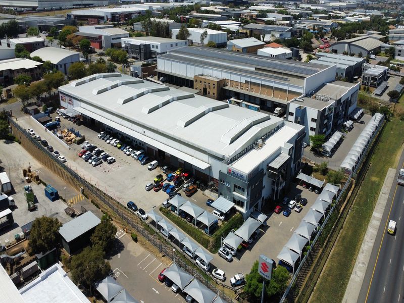 Aerial view of a large industrial warehouse facility featuring extensive parking, shade cloth carports, and dedicated loading bays within a commercial business park.