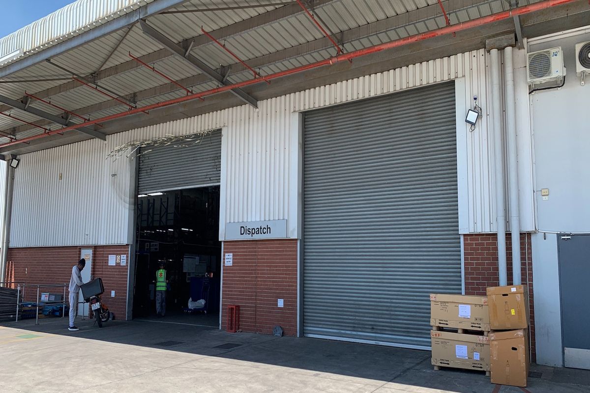 Industrial dispatch area featuring large roller shutter doors, corrugated metal and brick facade, and exposed fire suppression infrastructure.