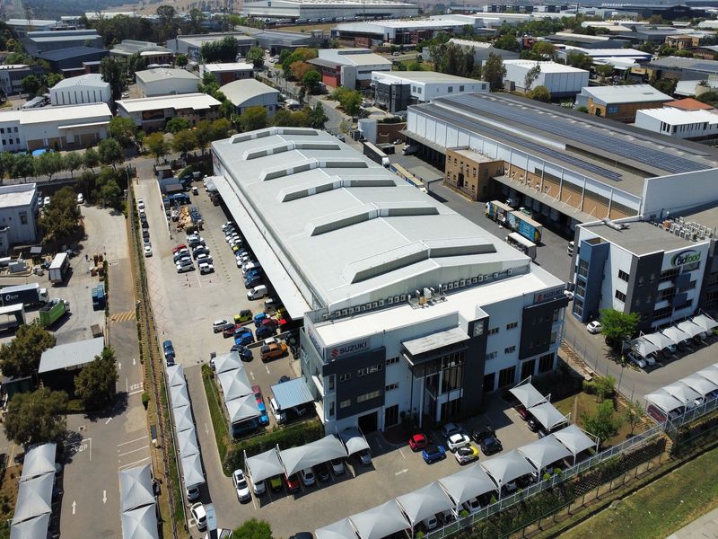 Aerial view of a large industrial warehouse facility featuring an integrated office block, extensive parking with shade cloth carports, and dedicated loading bays.