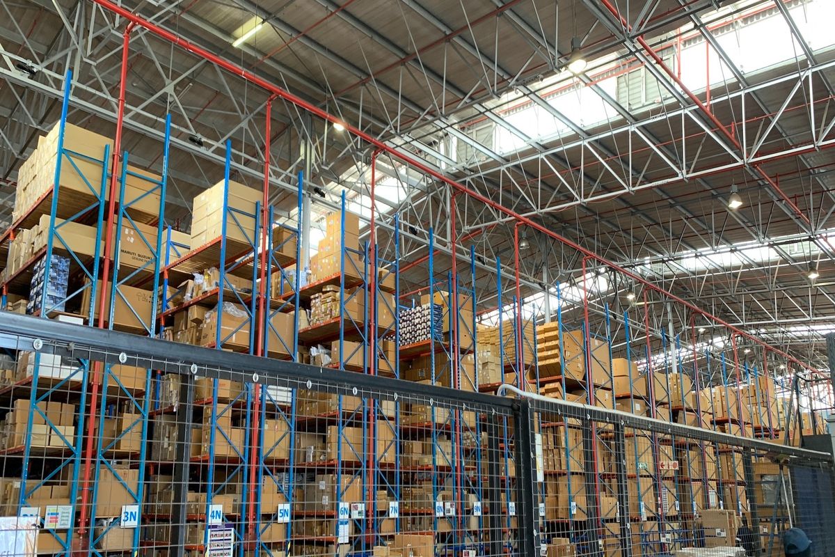 Industrial warehouse space featuring high-clearance steel racking systems, exposed roof trusses, integrated fire sprinkler infrastructure, and natural lighting through overhead skylights.