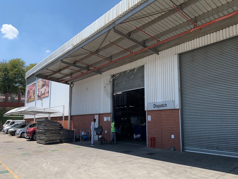 Industrial warehouse exterior featuring a dispatch loading bay with roller shutter doors, brick and metal cladding, and a concrete apron.
