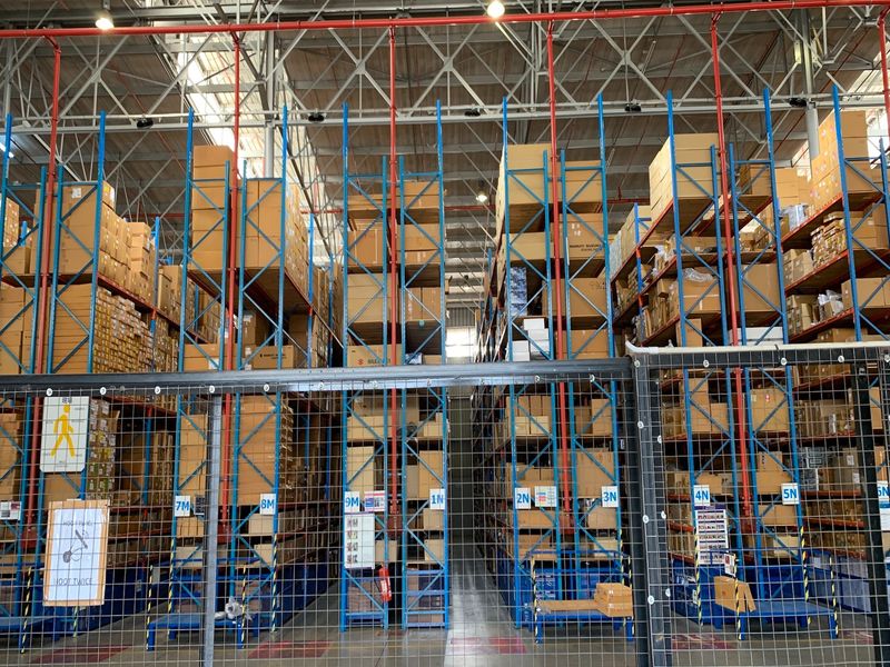Large industrial warehouse space featuring extensive steel racking systems, exposed roof trusses, and a functional fire sprinkler network.