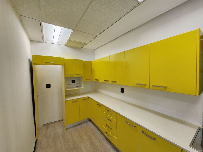 A clean, empty office kitchenette featuring bright yellow built-in cabinetry, white countertops, and modern drop ceiling lighting.