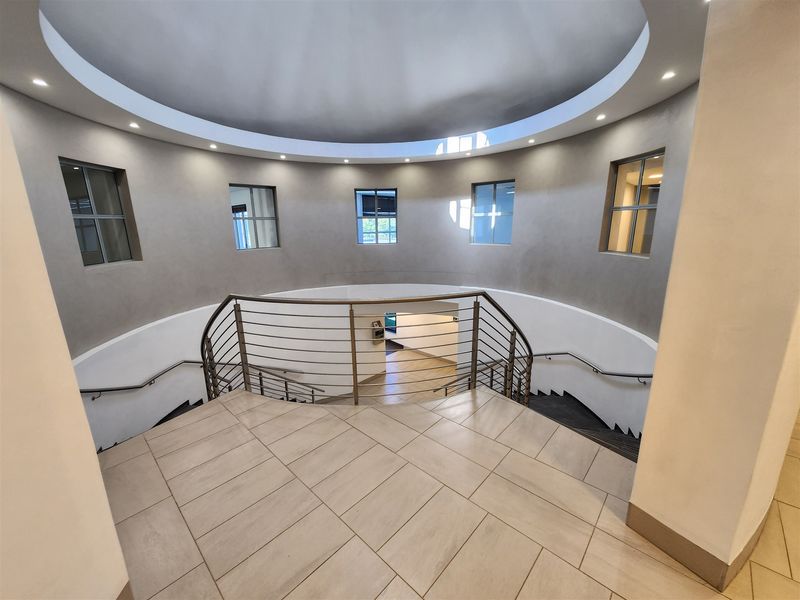 A modern, circular entrance foyer featuring a grand curved staircase with metal balustrades, tiled flooring, and elegant recessed dome ceiling lighting.