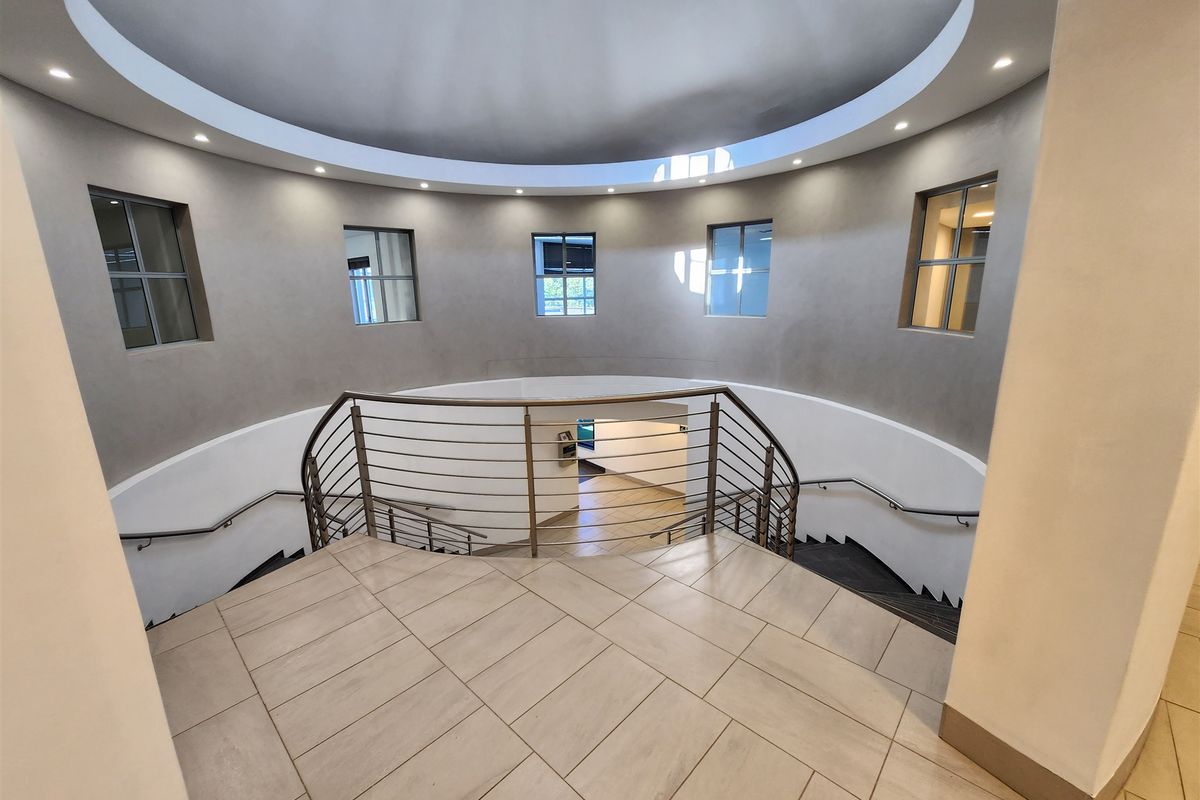 A modern, circular entrance foyer featuring a grand curved staircase with metal balustrades, tiled flooring, and elegant recessed dome ceiling lighting.