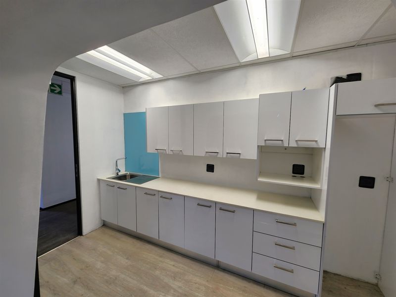 A clean and functional office kitchenette featuring white built-in cabinetry, a laminate countertop, stainless steel sink, and modern laminate flooring.