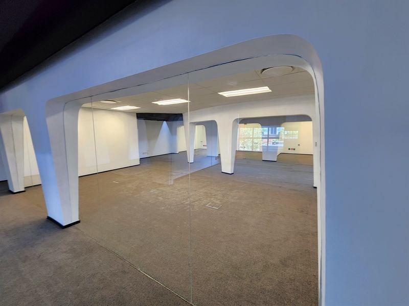 A spacious, open-plan office area featuring glass partitions, suspended ceilings with recessed lighting, and carpeted flooring with integrated floor power outlets.