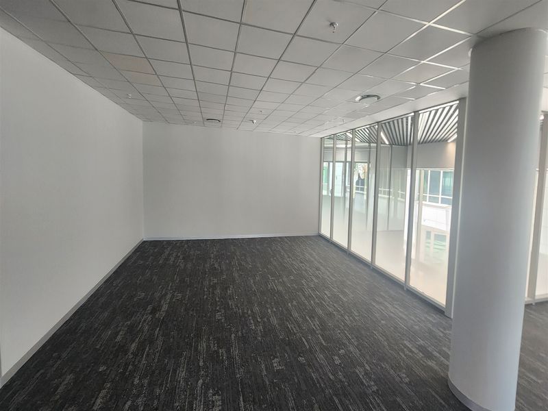 A bright, vacant office space featuring modern carpet tiles, a suspended ceiling, and a large glass partition wall providing natural light.