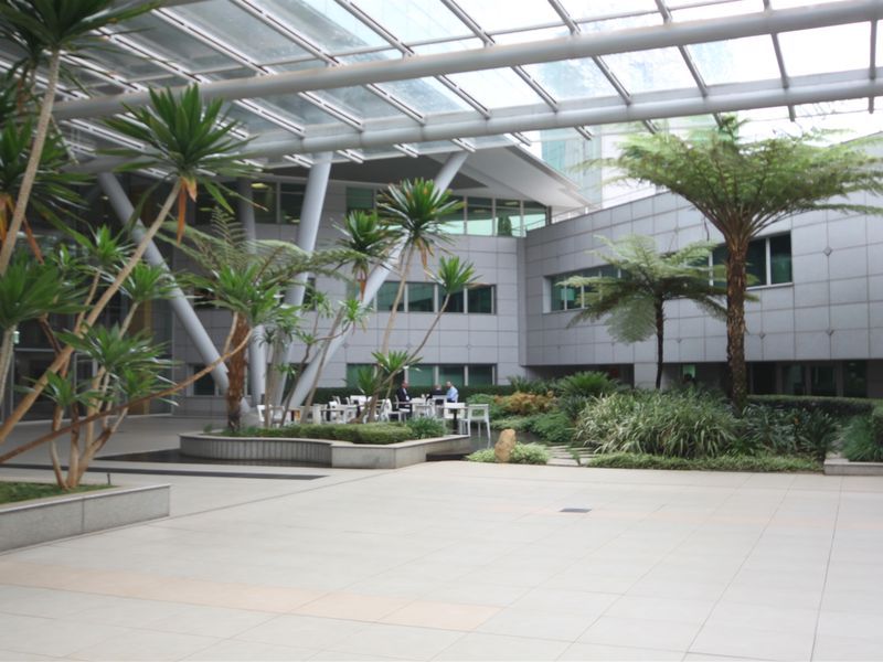 A spacious, modern office courtyard featuring a glass atrium roof, tiled flooring, and integrated landscaped planter beds.