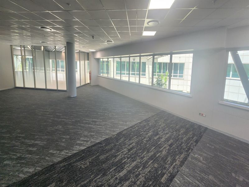 A spacious, open-plan office area featuring modern carpet tiles, suspended ceilings with recessed lighting, and extensive glass partitioning for a bright, professional workspace.