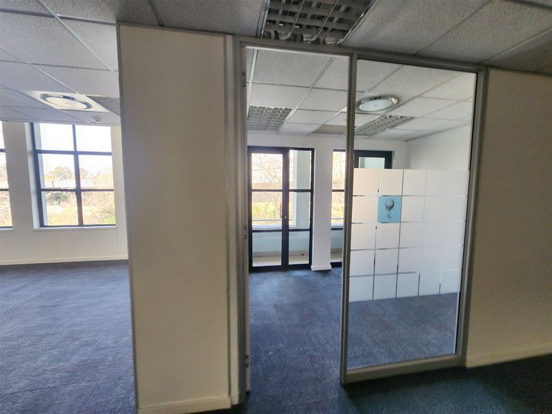 An empty office space featuring glass partitions, suspended ceilings, and large windows providing natural light and views.