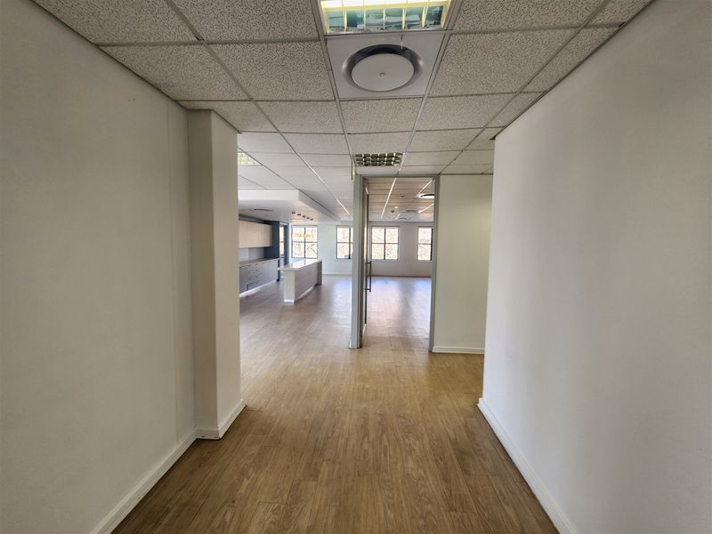 Spacious open-plan office area featuring laminate flooring, suspended ceilings with recessed lighting, and a functional kitchenette counter, offering a clean and professional workspace.