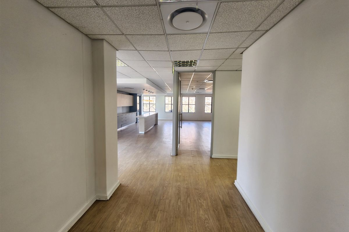 Spacious open-plan office area featuring laminate flooring, suspended ceilings with recessed lighting, and a functional kitchenette counter, offering a clean and professional workspace.