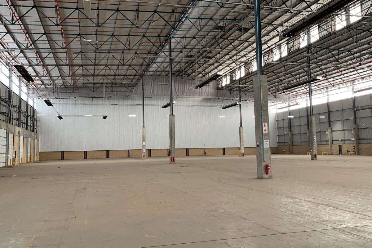Spacious industrial warehouse featuring high ceilings with exposed steel trusses, concrete flooring, and multiple roller shutter doors for efficient logistics and storage operations.