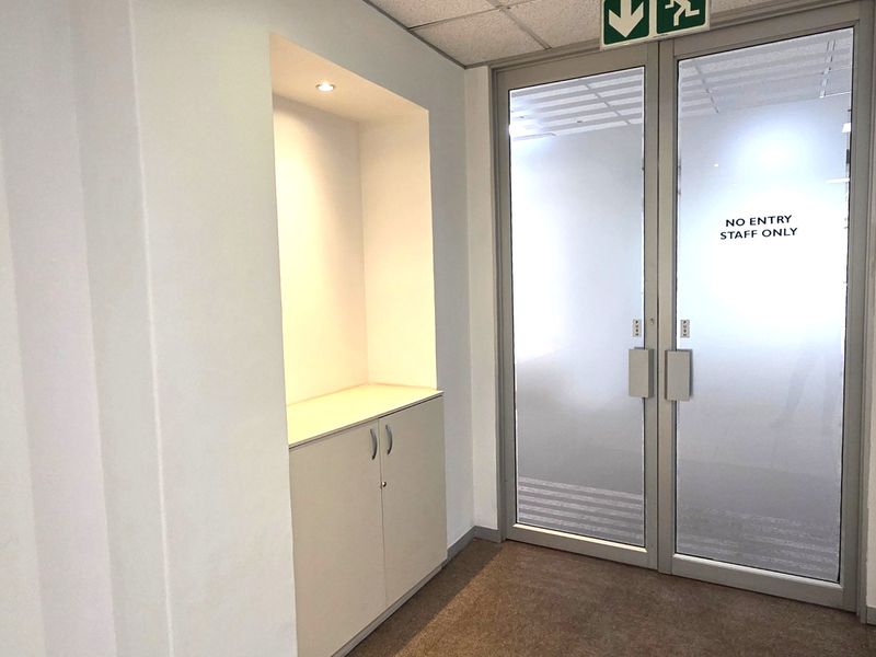 A clean office hallway featuring built-in cabinetry, recessed lighting, and frosted glass double doors with staff access signage.