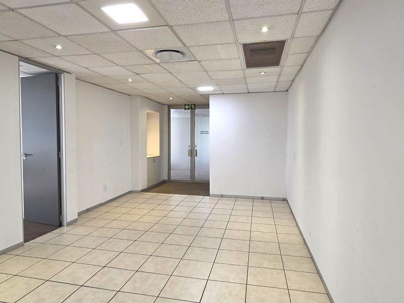 A bright, vacant office space featuring tiled flooring, a suspended ceiling with recessed lighting, and integrated air conditioning.