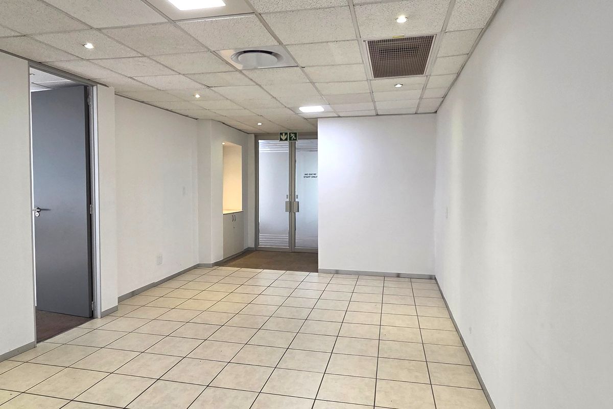 A bright, vacant office space featuring tiled flooring, a suspended ceiling with recessed lighting, and integrated air conditioning.