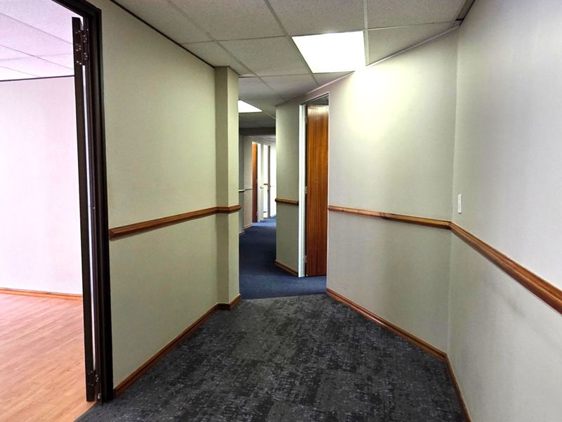 A clean, functional office hallway featuring neutral walls, wooden dado rails, carpeted flooring, and recessed lighting, providing access to multiple office rooms.