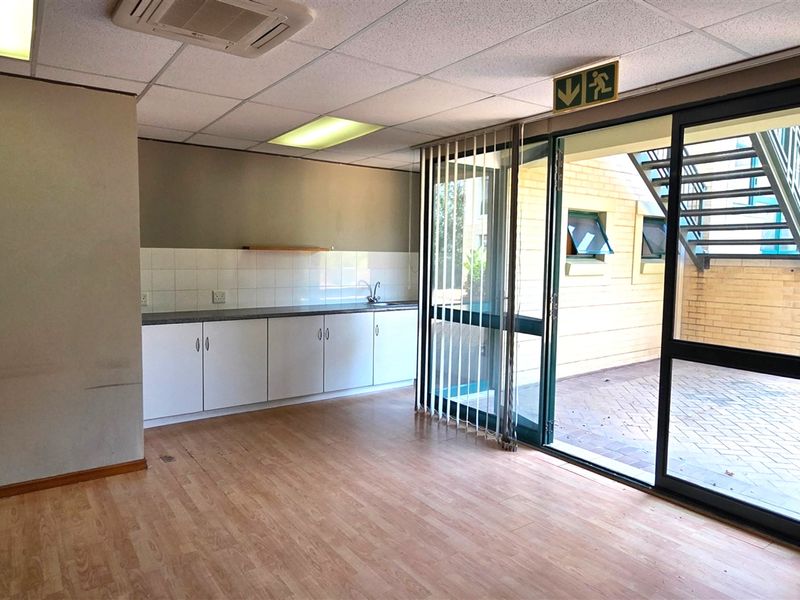 An empty office space featuring a built-in kitchenette, laminate flooring, suspended ceiling, and direct access to an outdoor area through a sliding glass door.
