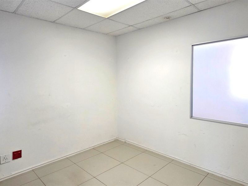 A vacant office space featuring tiled flooring, a suspended ceiling with recessed lighting, and a fixed window, ready for customization.
