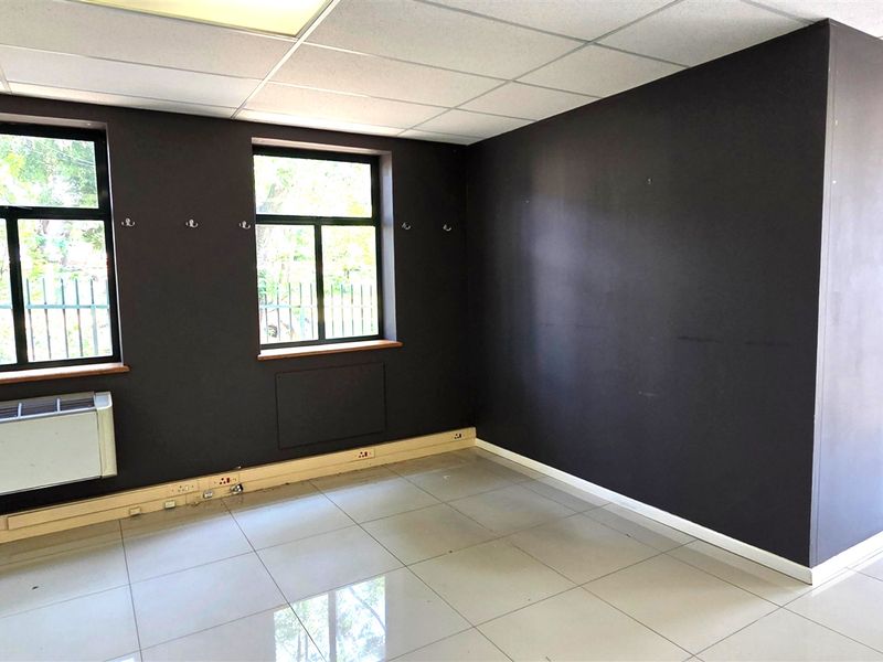 A vacant office space featuring dark painted walls, tiled flooring, a suspended ceiling, and integrated air conditioning, suitable for a professional workspace.