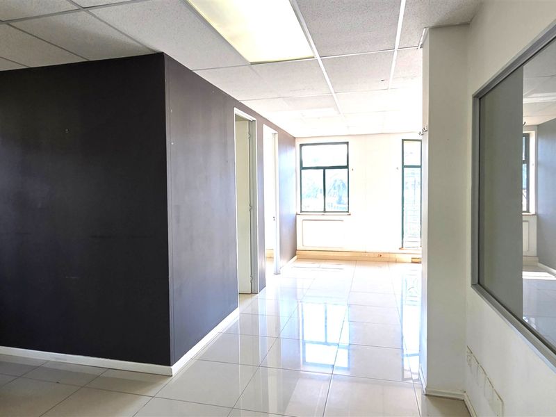 An empty office space featuring tiled flooring, a suspended ceiling with recessed lighting, and large windows providing natural light.