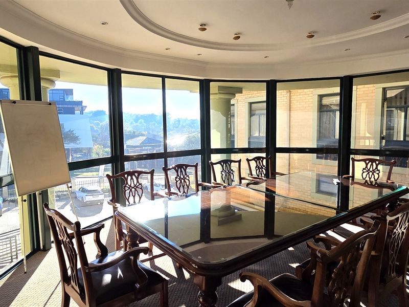A professional office space featuring large floor-to-ceiling windows, recessed ceiling lighting, and a curved architectural design, providing ample natural light.