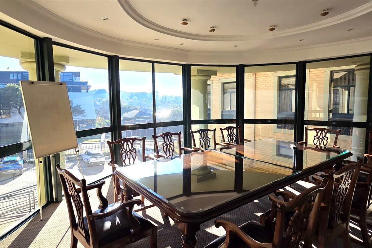 A professional office space featuring large floor-to-ceiling windows, recessed ceiling lighting, and a curved architectural design, providing ample natural light.