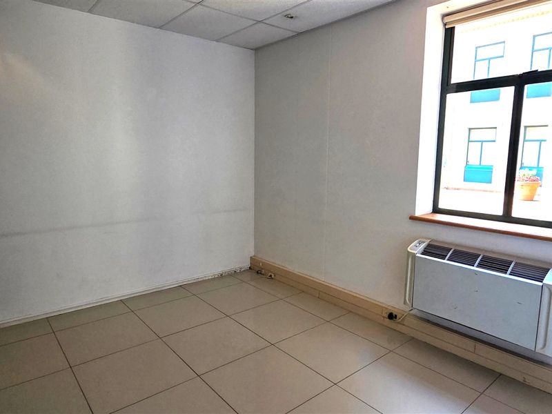 A vacant office space featuring tiled flooring, a suspended ceiling, and a wall-mounted HVAC unit, offering a clean and functional workspace environment.