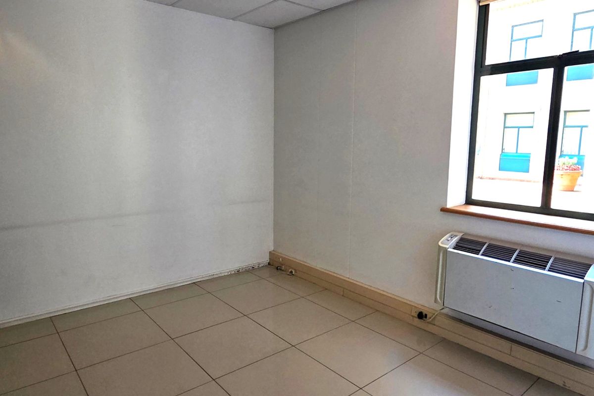 A vacant office space featuring tiled flooring, a suspended ceiling, and a wall-mounted HVAC unit, offering a clean and functional workspace environment.