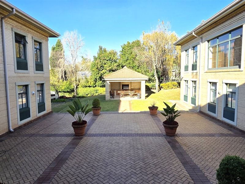A well-maintained courtyard area between office buildings featuring brick paving, a central garden path, and a covered outdoor entertainment structure with a built-in braai.