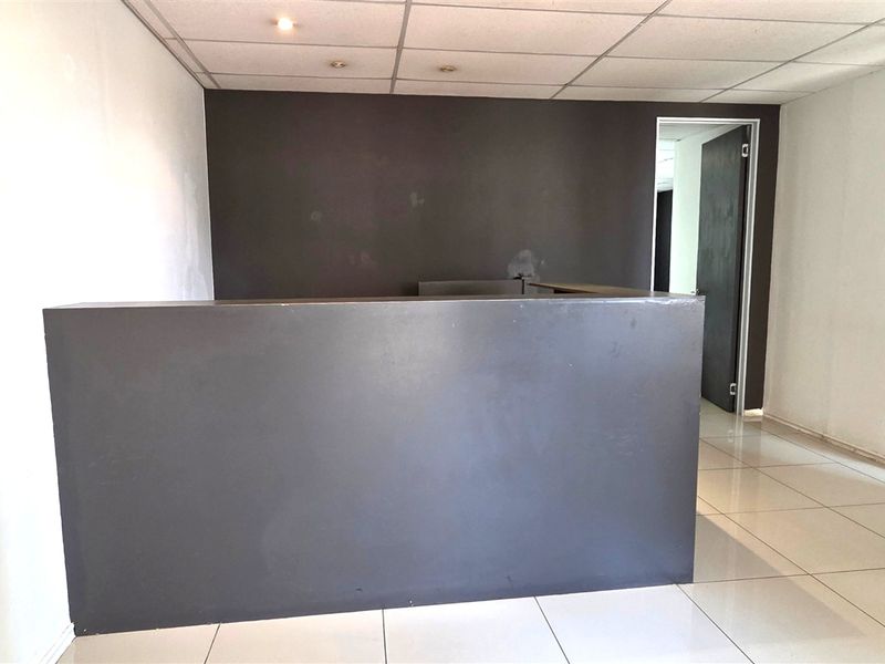 An empty office space featuring a built-in reception desk, tiled flooring, and a suspended ceiling with recessed lighting.