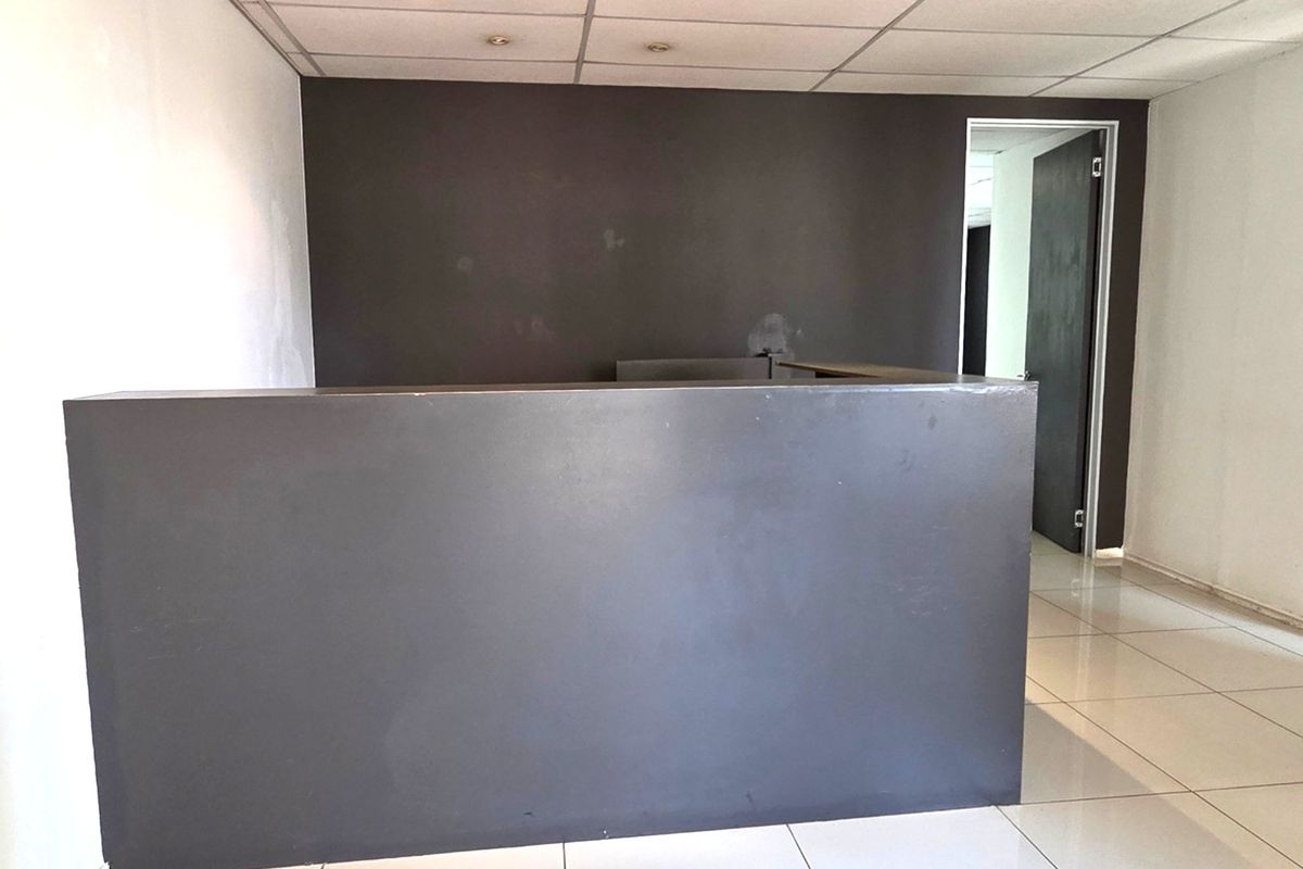 An empty office space featuring a built-in reception desk, tiled flooring, and a suspended ceiling with recessed lighting.