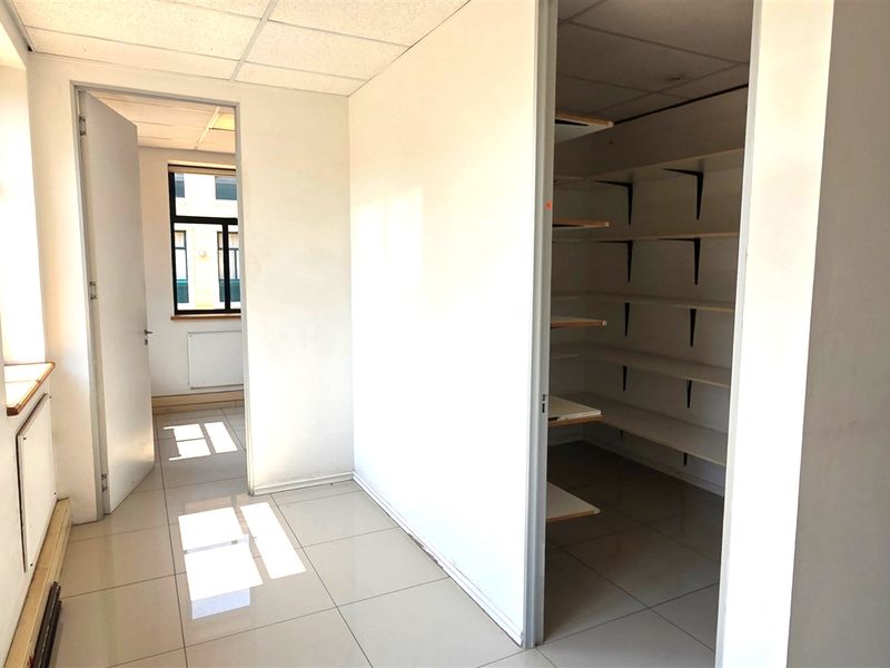An empty office space featuring tiled flooring, a suspended ceiling, and a dedicated storage area with built-in shelving.