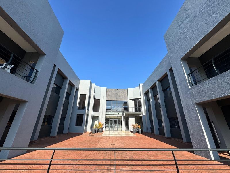 A modern office building courtyard featuring a paved central area, glass entrance facade, and symmetrical multi-level office wings with balconies.