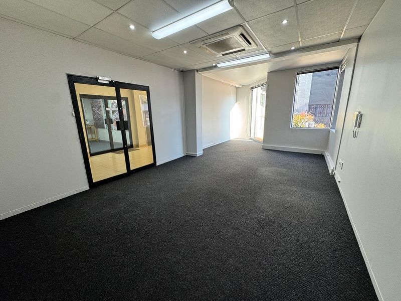 A bright, empty office space featuring carpeted flooring, a suspended ceiling with integrated lighting, ducted air conditioning, and glass-panelled double doors.