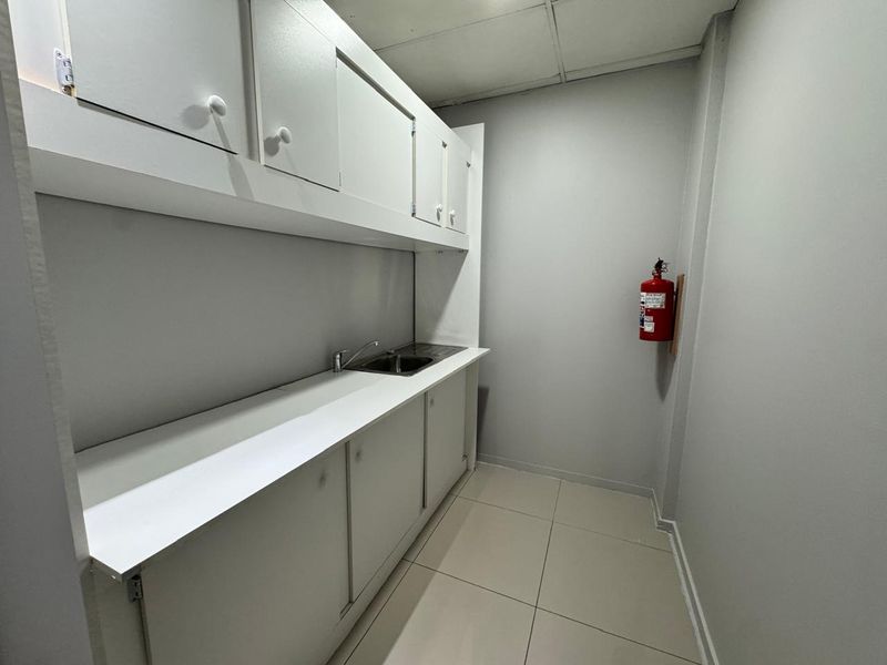 A functional office kitchenette featuring built-in white cabinetry, a stainless steel sink, and tiled flooring, providing a clean and practical utility space.