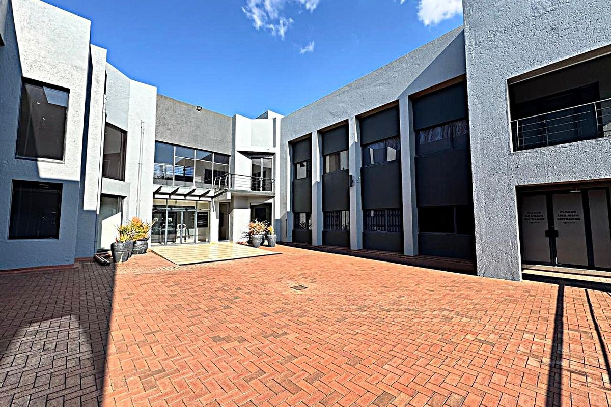 A spacious paved courtyard area featuring a modern office building facade with large glass windows and metal balcony railings.