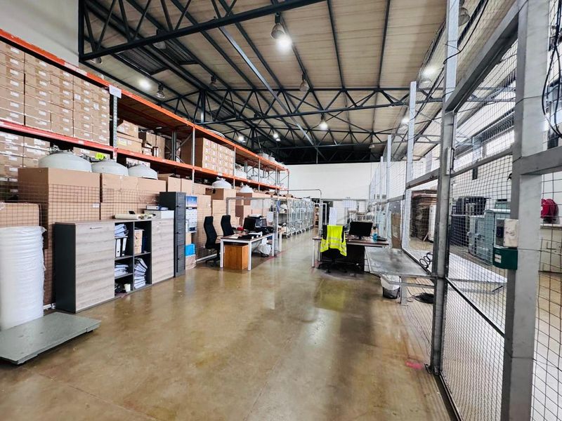 Spacious industrial warehouse area featuring high exposed steel roof trusses, concrete flooring, and extensive built-in racking systems for storage.
