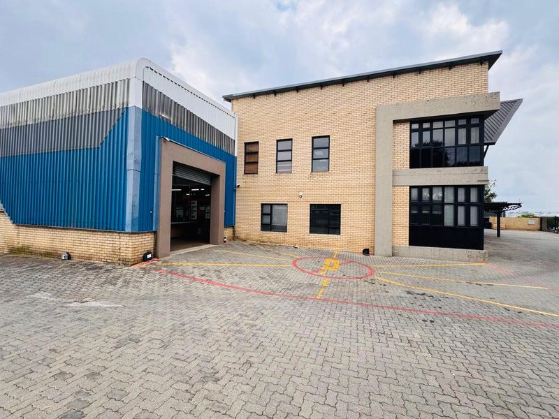 Industrial property exterior featuring a combination of brick office facade and metal-clad warehouse section with a roller shutter door and paved yard area.