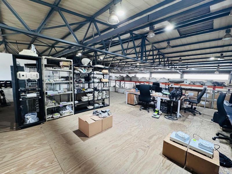 Spacious industrial utility area featuring exposed steel roof trusses, high-bay lighting, and durable plywood flooring, currently utilized for storage and workspace.