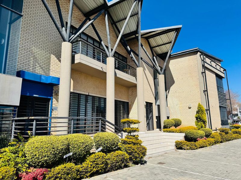 Front elevation of a modern industrial building featuring brick facade, prominent steel support columns, a balcony, and well-maintained landscaped garden areas.