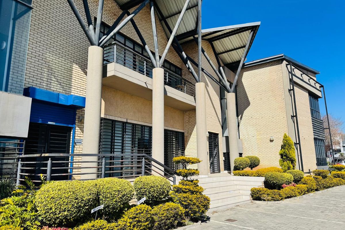 Front elevation of a modern industrial building featuring brick facade, prominent steel support columns, a balcony, and well-maintained landscaped garden areas.