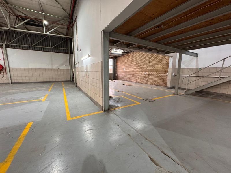 Spacious industrial utility area featuring exposed steel trusses, mezzanine level with staircase, tiled wall sections, and durable painted concrete flooring.
