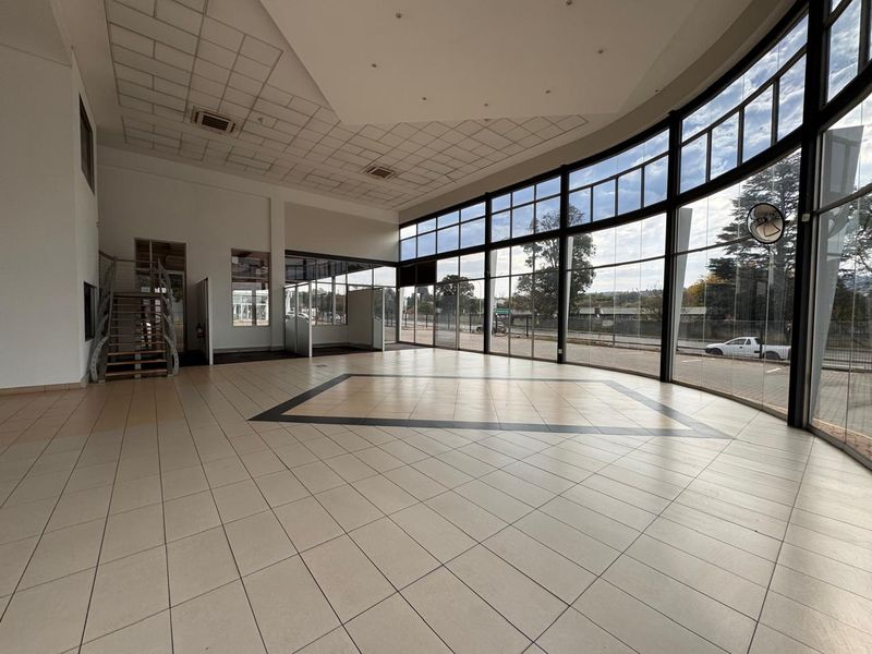 Spacious open-plan retail showroom featuring extensive floor-to-ceiling glass frontage, tiled flooring, and a modern staircase, offering excellent natural light and visibility.