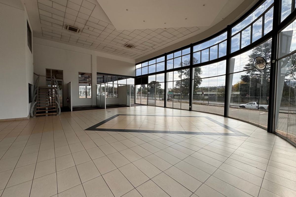 Spacious open-plan retail showroom featuring extensive floor-to-ceiling glass frontage, tiled flooring, and a modern staircase, offering excellent natural light and visibility.